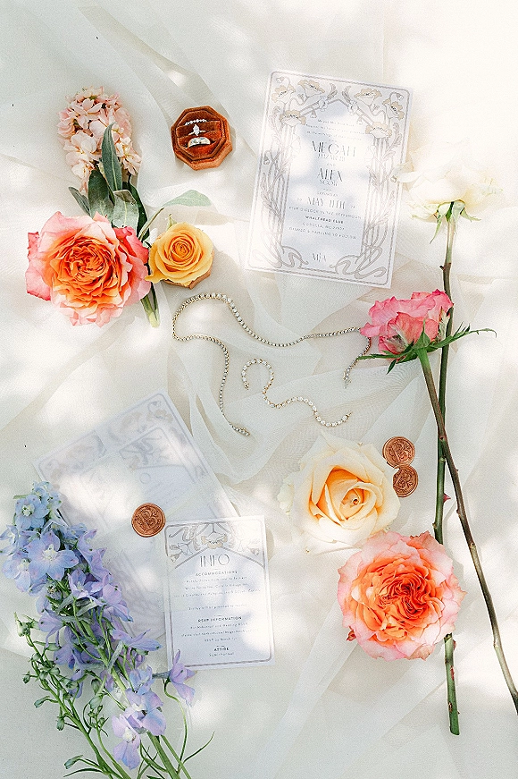 Invitation suite wedding invitation flat lay with wax seal, velvet ring box, rings, pearls and pastel florals on white fabric backdrop