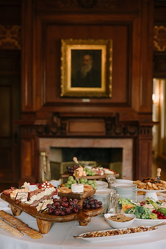 Wedding grazing table loaded with charcuterie table wedding boards of cheese, salami, crackers and grapes in a wood-paneled room by a fireplace