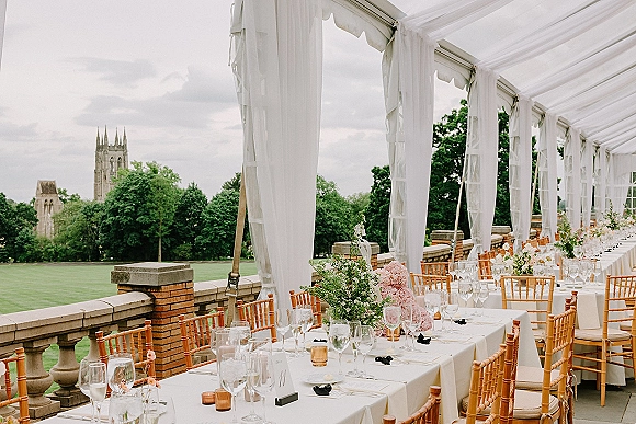 Reception tablescape with long banquet table wedding setup, white linens, florals and votives under a draped tent on a terrace balcony