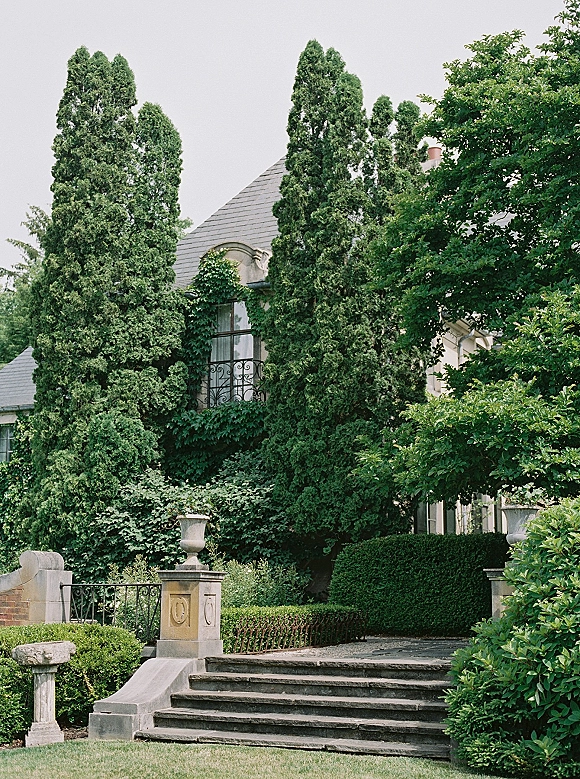 Wedding venue exterior at an estate wedding venue with ivy vines on the mansion facade, stone steps, and a wrought iron railing amid hedges