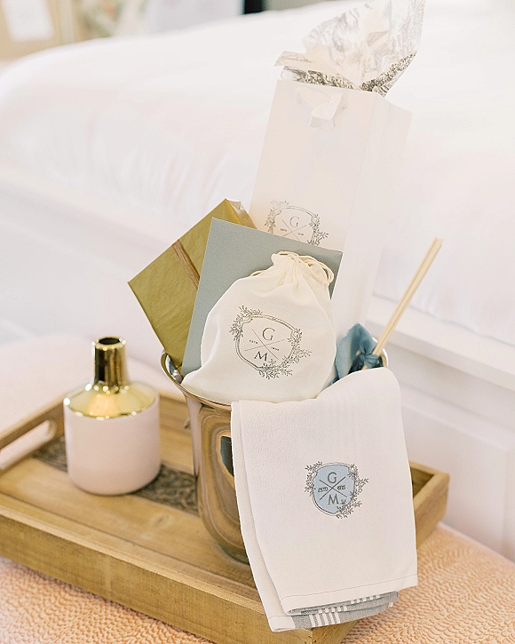Welcome gift bags with tissue paper, monogram label, and note cards arranged on a wooden tray beside a white sofa in a neutral room interior