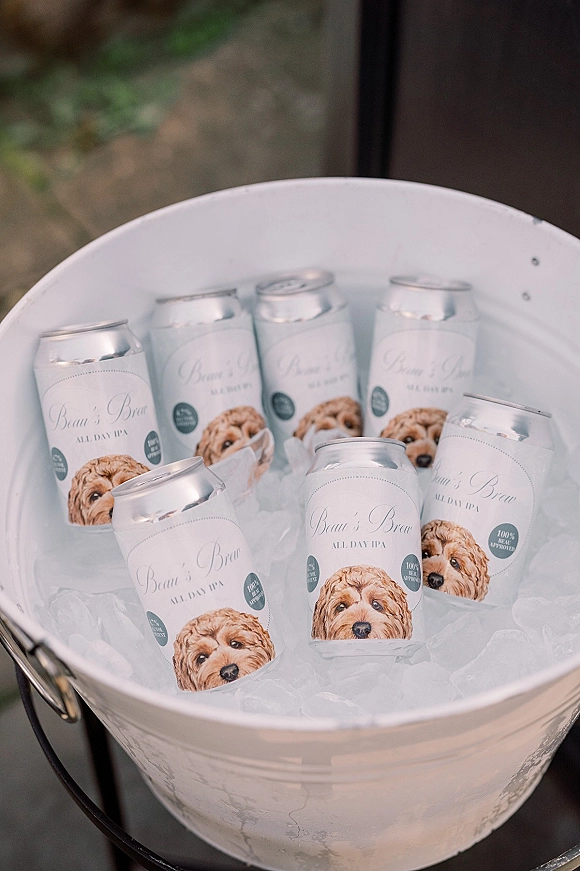 Wedding beer display with beer bucket with ice, canned beers in a white metal tub and bottle opener by a glass door patio walkway