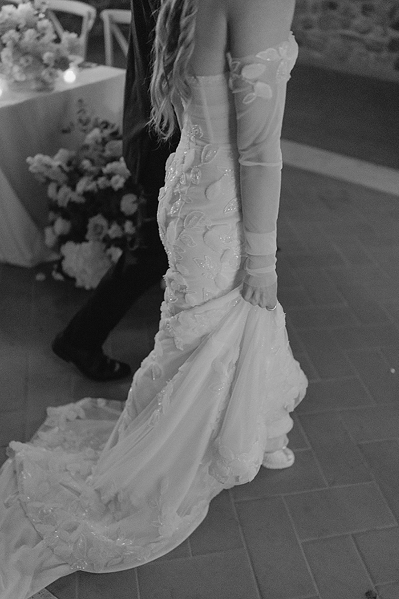 Wedding dress in strapless lace with mermaid silhouette and long train, paired with sheer opera gloves and ring near candlelit reception table