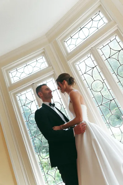 Couple portrait, an indoor wedding portrait framed by leaded glass windows and garden greenery, with the groom's black bow tie as a crisp accent.