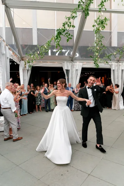 Wedding first dance becomes a grand entrance dance as the couple twirls under string lights in a clear tent with guests cheering.