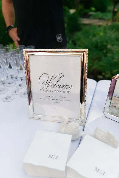 Wedding welcome sign, a framed wedding sign set on a white tablecloth with porcelain swan figurines, against lush garden greenery.