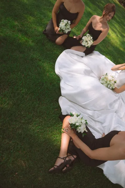 Bridal party portrait of a bride with bridesmaids seated together, each holding simple white rose bouquets.