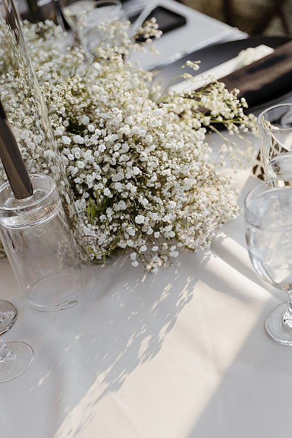 Wedding tablescape with baby’s breath centerpiece in a clear glass vase, set on a white tablecloth with glassware at the reception table