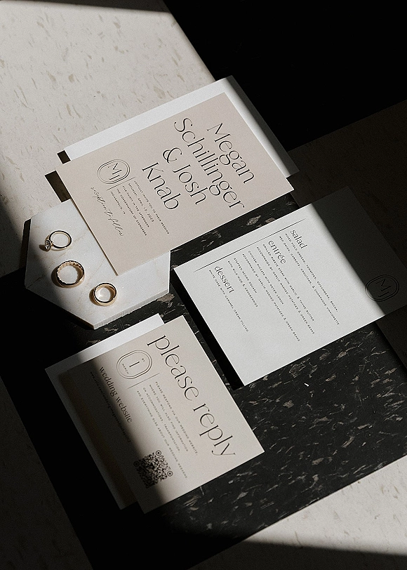 Wedding invitation suite, modern wedding invitations arranged with RSVP card, wax-sealed envelope, and rings on dark marble with shadows
