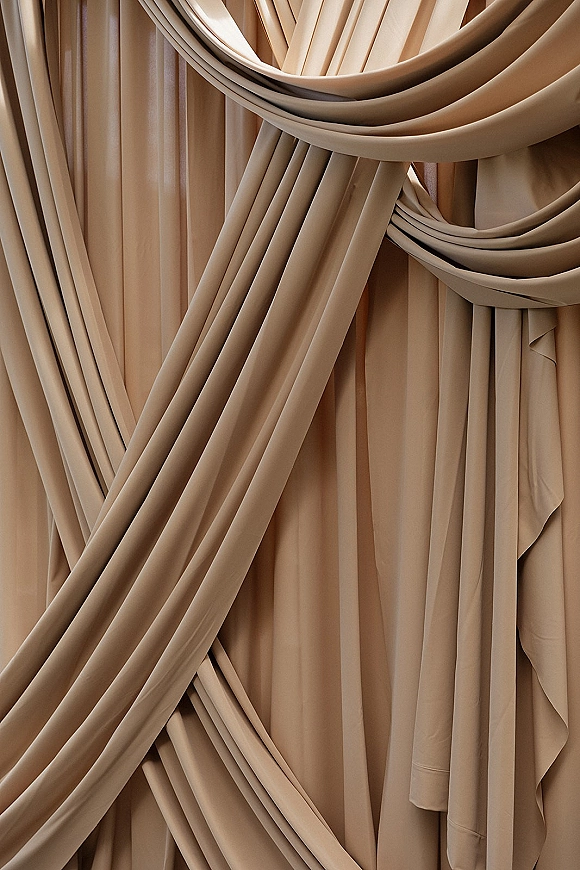 Wedding drapery backdrop with neutral wedding draping, showing pleated layered folds and a knotted detail on a fabric wall