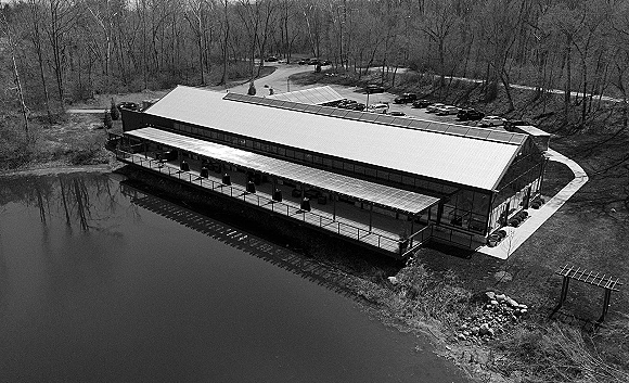 Wedding venue exterior with a metal roof and covered patio, set by a lakefront wedding venue with glass walls and wooded trees beyond