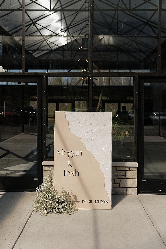 Wedding welcome sign with modern wedding welcome sign serif text, plaster texture and baby's breath greenery, set by a glass facade entrance