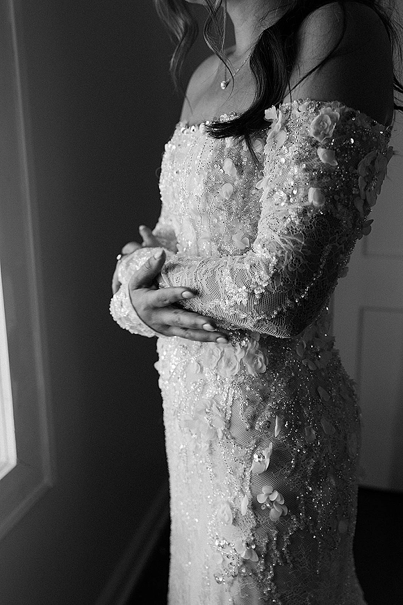Wedding dress close-up of a beaded wedding dress with sequin lace, 3D floral appliques and long sleeves, glowing in window light
