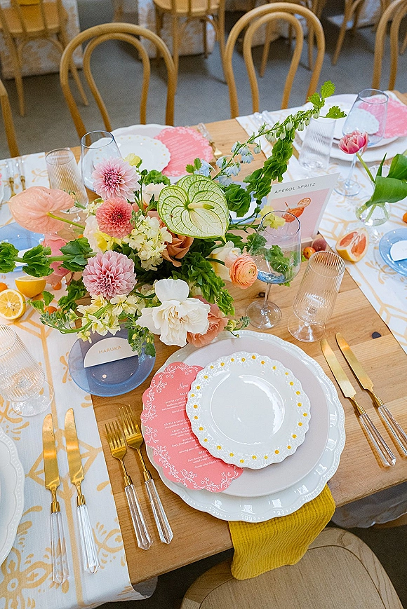Reception tablescape with colorful wedding tablescape blooms and citrus slices, scalloped plates, blue glass chargers, gold flatware on wood table