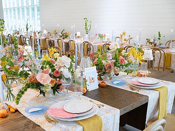 Reception tablescape with colorful wedding tablescape details, taper candles, floral centerpieces, citrus, and patterned linens in a bright banquet room