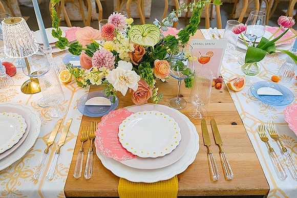 Reception tablescape with colorful wedding tablescape details, pastel tulips and anthurium, taper candles, gold flatware, and fruit on patterned linen