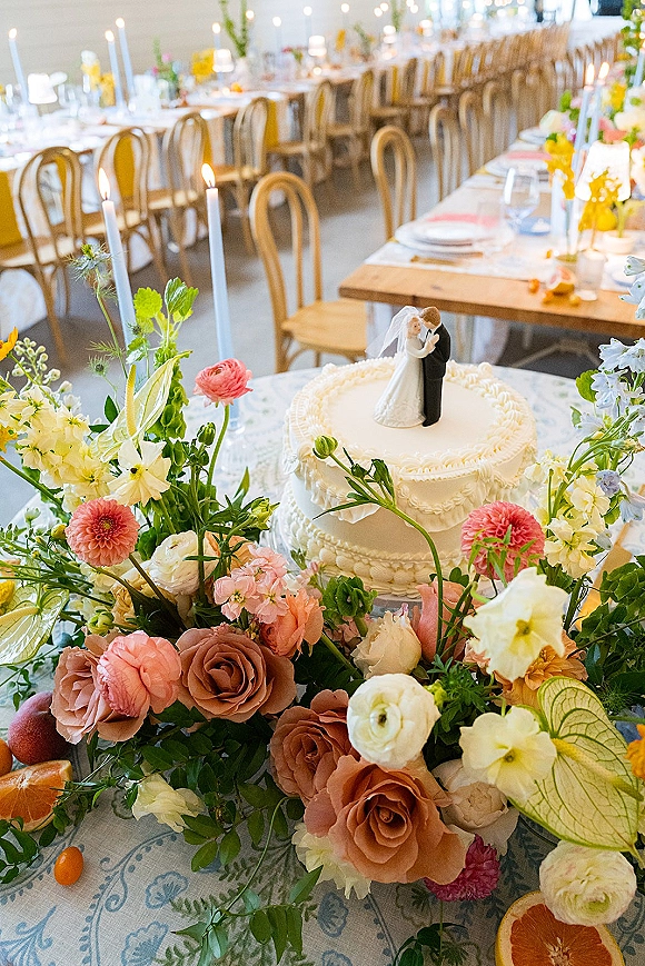 Wedding cake with buttercream wedding cake finish, topped with roses and taper candles on a linen table under string lights in a tent reception