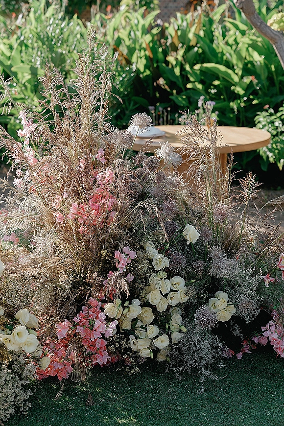 Ceremony floral arrangement with a ground floral installation of white roses, pink blooms and dried grasses on a sunny garden lawn