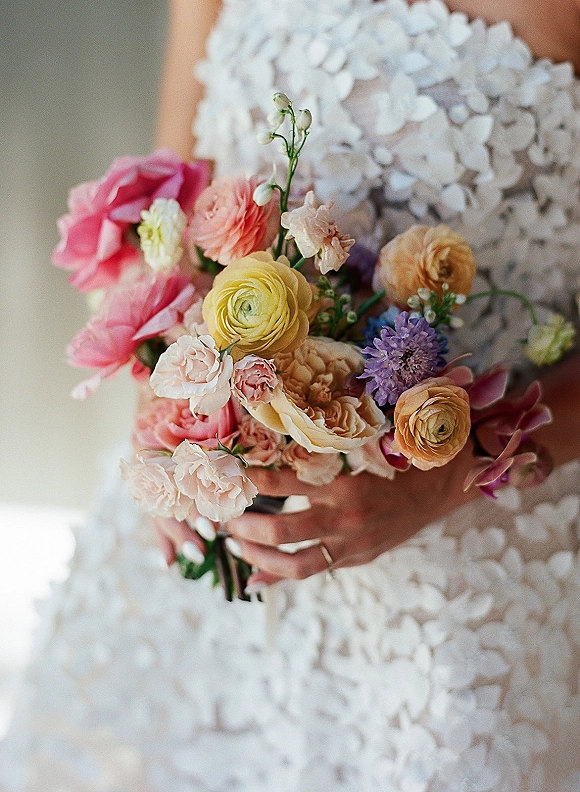 Bridal bouquet of garden rose bouquet with ranunculus, purple scabiosa and greenery held by bride in floral appliqué gown, soft light