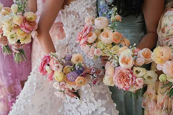 Bridesmaid bouquets with pastel bridesmaid bouquets of garden roses, ranunculus, and greenery held by women standing together indoors