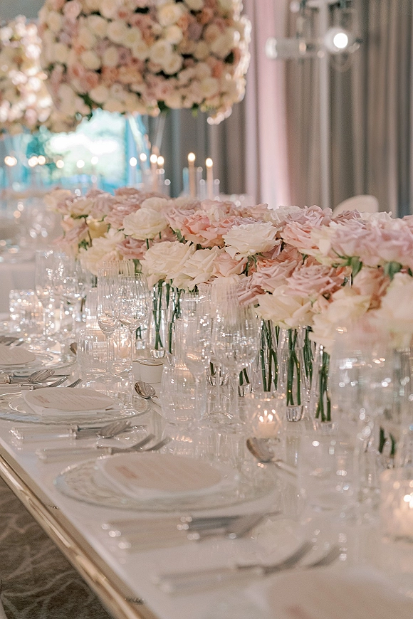 Reception tablescape wedding table decor with blush and ivory florals, bud vases, taper and votive candles, and formal place settings in a draped banquet room