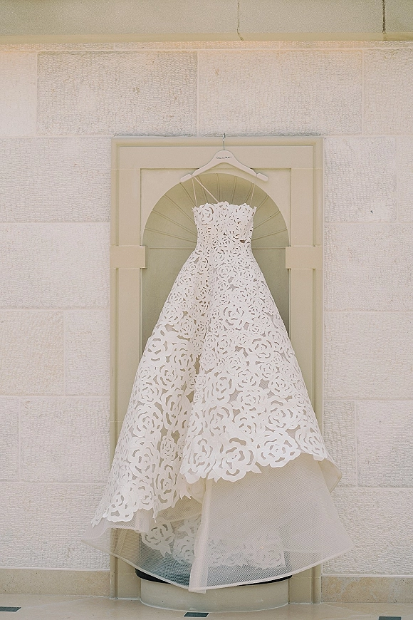 Wedding dress with strapless wedding dress lace bodice on a hanger, showing floral applique and tulle underskirt against a stone wall niche