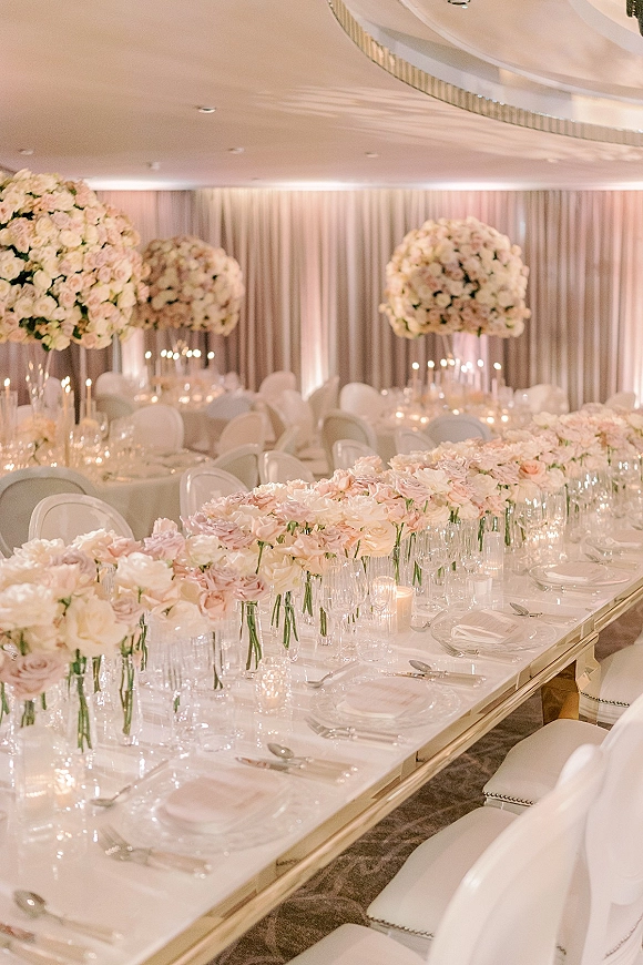 Reception tablescape with pink and white florals, candlelit glass votives, crystal glassware, and mirrored table in a draped ballroom