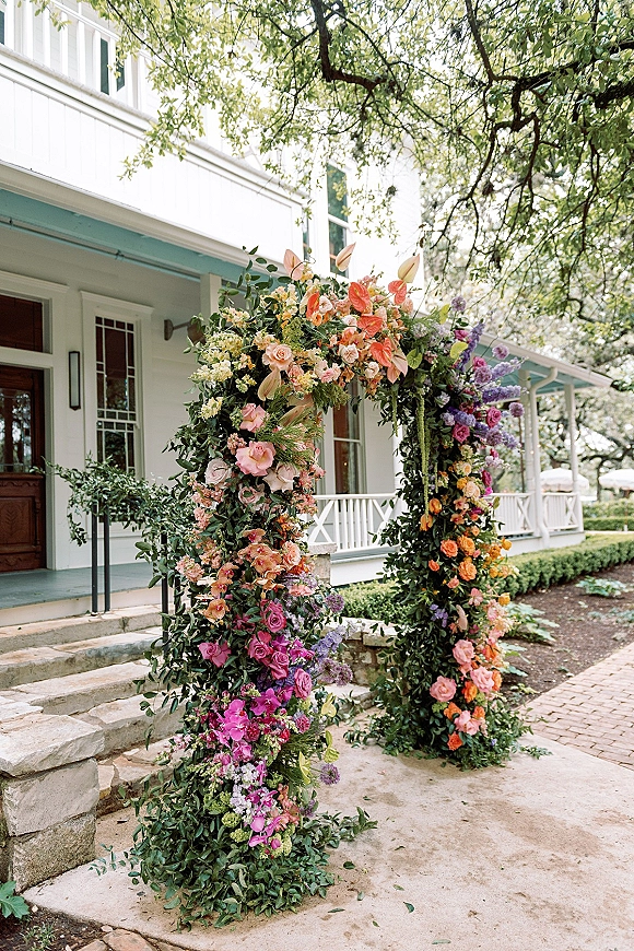 Floral wedding arch with a colorful wedding arch design of roses, orchids, anthurium, and greenery on a white house porch steps