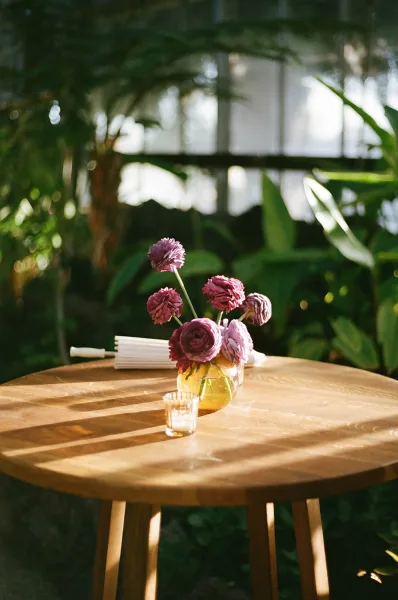 Wedding centerpiece with a small floral arrangement in a glass vase and a single votive candle on a wood table in a greenhouse setting