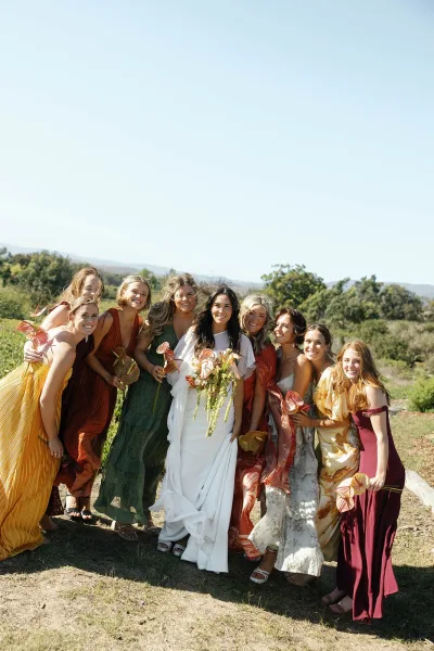 Bridesmaid group photo with bride and bridesmaids holding anthurium bouquets, standing in a hillside meadow with mountains under blue sky