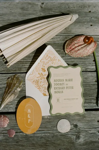 Wedding invitation suite with scalloped wedding invitation, wax seal and ribbon, styled with seashells on a weathered wood table