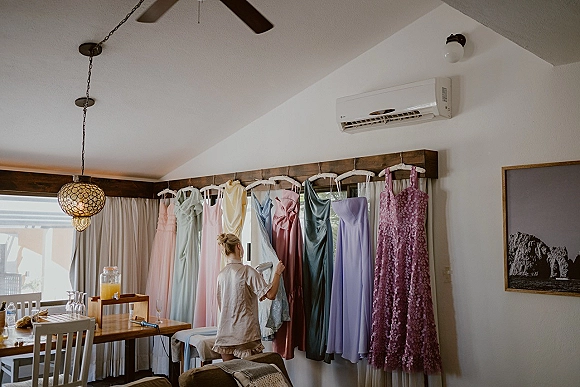 Bridesmaid dresses in a bridesmaid dress lineup on hangers along a clothing rack in a bridal suite, with a pendant light overhead