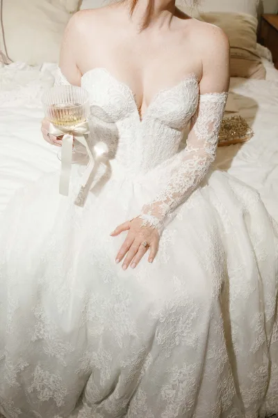 Wedding dress close-up of a lace wedding dress with a champagne coupe tied with ribbon nearby, suggesting an intimate getting-ready moment.