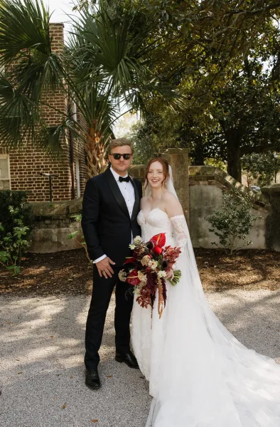 Couple portrait as a garden wedding portrait framed by palm trees, bride holding a bouquet beside a brick wall