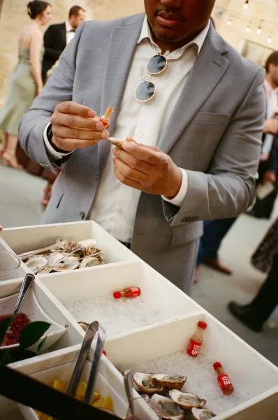 Oyster bar anchoring the cocktail hour raw bar, lemon wedges ready as guests mingle under string lights by a stone wall.