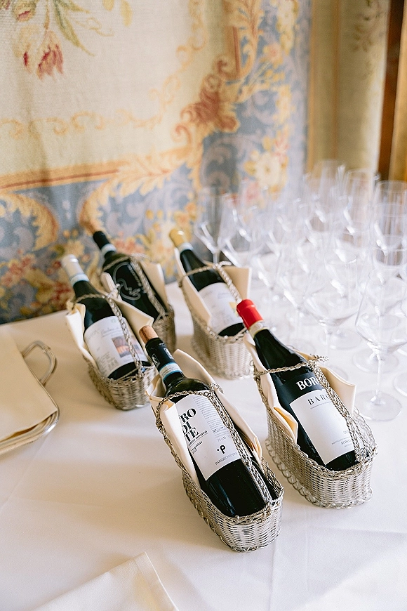 Wedding wine service with wine bottle presentation in woven baskets, napkins and filled glasses on a white tablecloth before a mural wall backdrop