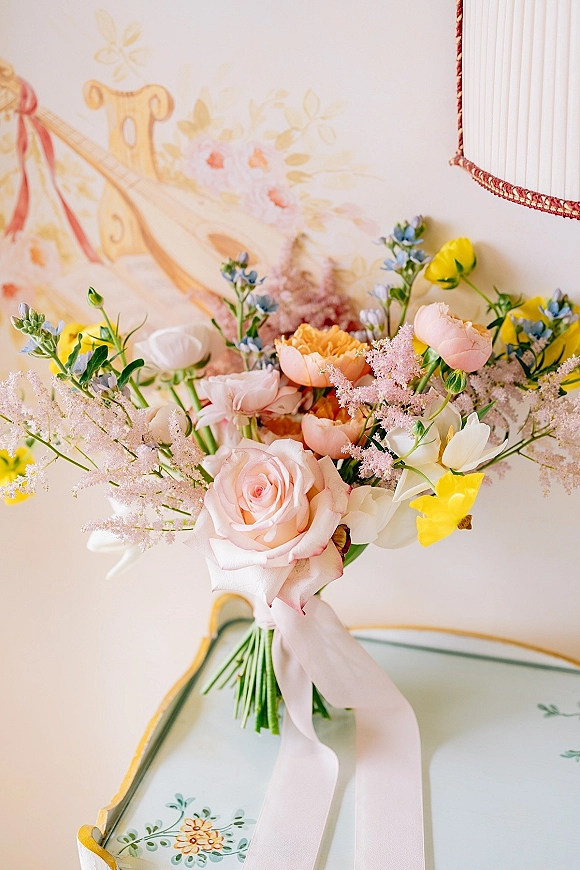 Bridal bouquet of pastel bridal bouquet roses with a ribbon bow, styled against a painted wall mural with a wall lamp and tray