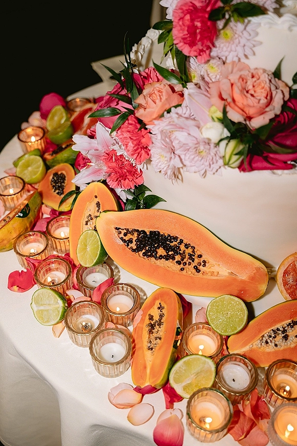 Wedding tablescape with tropical wedding tablescape flair, featuring papaya halves, limes, votive candles, rose petals, and gold holders on white linen