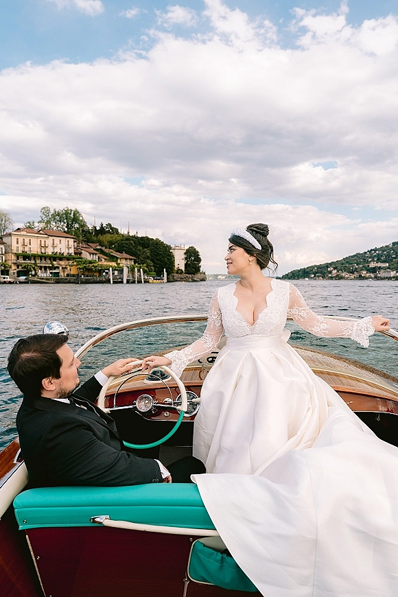 Couple portrait of wedding couple on boat, bride in lace long-sleeve dress and headband with groom in tux beside teal seats on lake