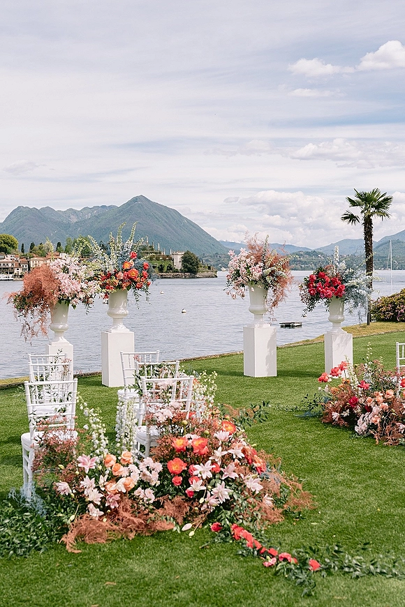 Ceremony setup for an outdoor wedding ceremony with white chairs and aisle flowers on a lakeside lawn with mountain views
