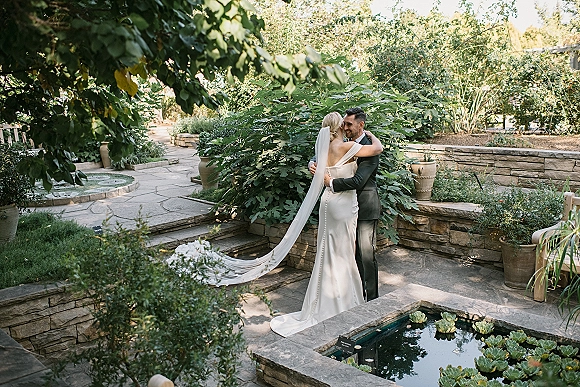 Couple portrait in a garden wedding portrait, bride and groom embrace on a stone patio by a reflecting pool with water lilies and greenery