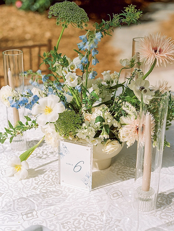 Wedding centerpieces with garden style centerpiece of white, blue, and blush blooms in glass cylinders and ceramic vase, taper candles on patterned linen