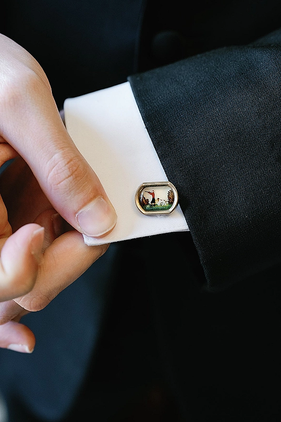 Wedding cufflinks on a groom’s white shirt cuff and dark suit jacket, shown in a cufflink close up with a hand adjusting them