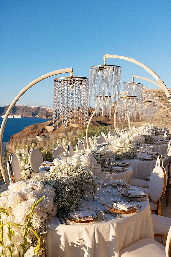 Reception tablescape with an outdoor reception table set in white and gold, hydrangea centerpieces, candlelight, and cliffside ocean views
