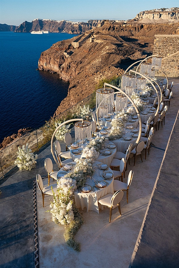 Reception tablescape with outdoor reception table styling, white florals and baby’s breath garland under crystal lanterns on a cliffside ocean terrace