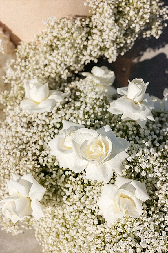 Bouquet close-up of white rose bouquet with baby’s breath accents resting on a stone surface, soft shadows highlighting petals and texture