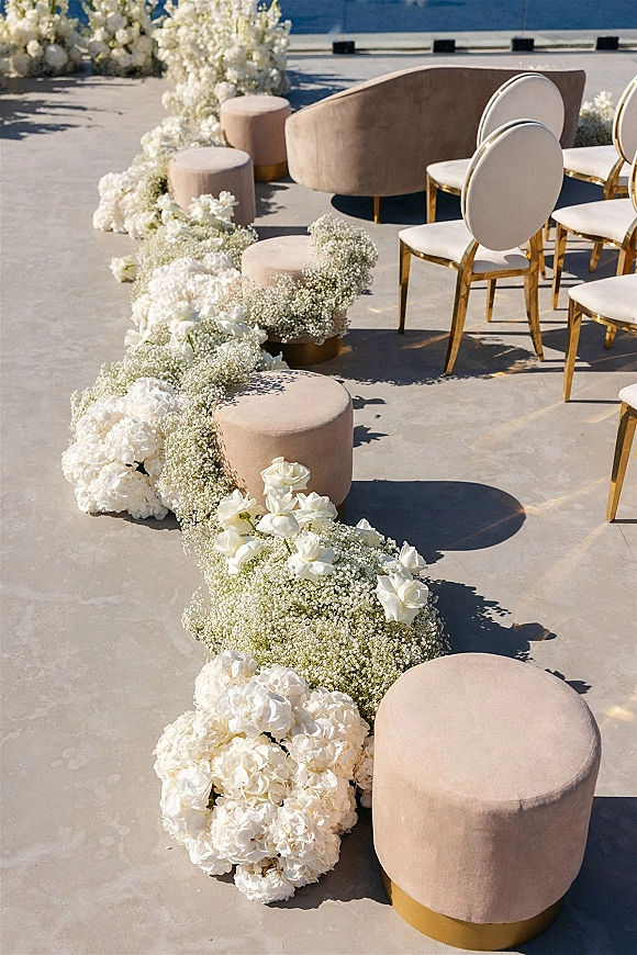 Ceremony aisle decor with floral aisle runner of white roses, hydrangeas, and baby’s breath on a stone patio overlooking the ocean
