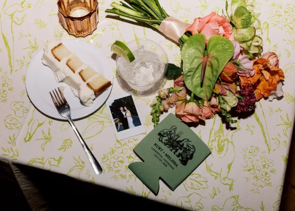 Wedding flat lay showcasing reception table details with a buttercream cake slice arranged on patterned table linen.