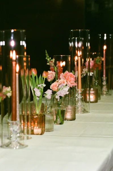 Reception tablescape glows as a candlelit wedding table with taper candles, set against a dark indoor backdrop.