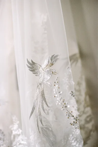 Wedding veil detail of an embroidered tulle veil showcasing a graceful bird motif, fine stitches across airy layers.